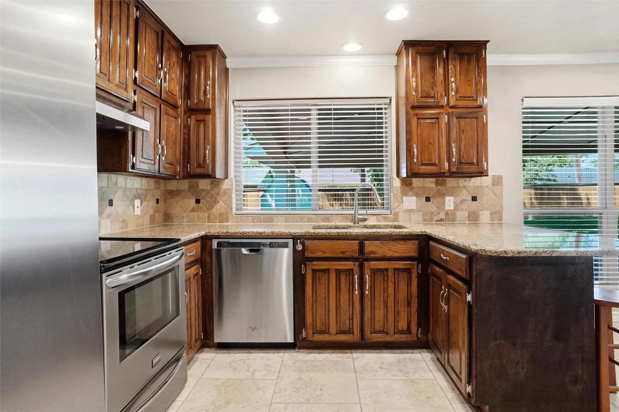Kitchen featuring wood cabinetry, stainless steel appliances, speckled countertops, tile flooring, and a tile backsplash