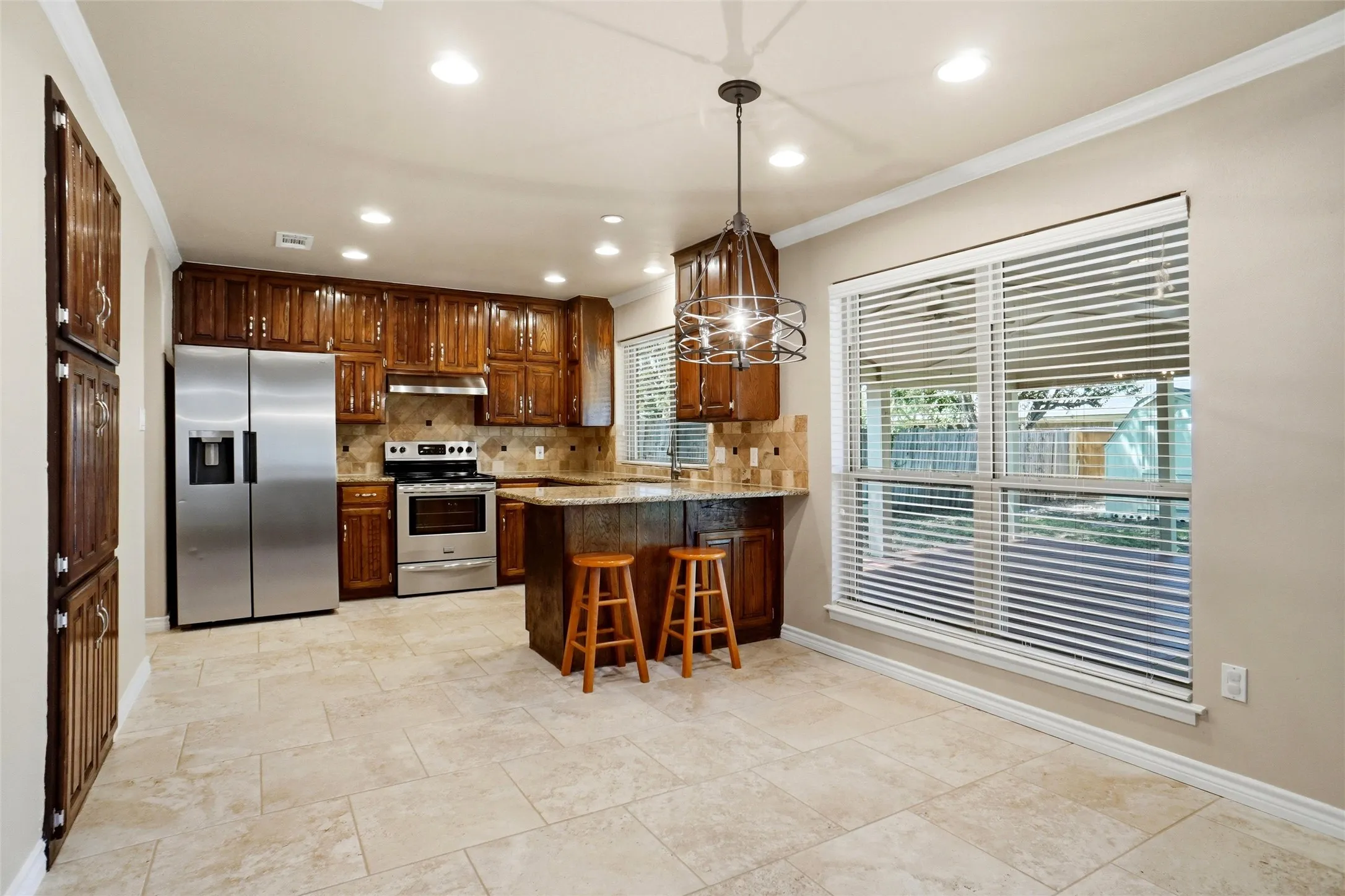 Kitchen with tile flooring, wood cabinetry, stainless steel appliances, and a central island with a breakfast bar