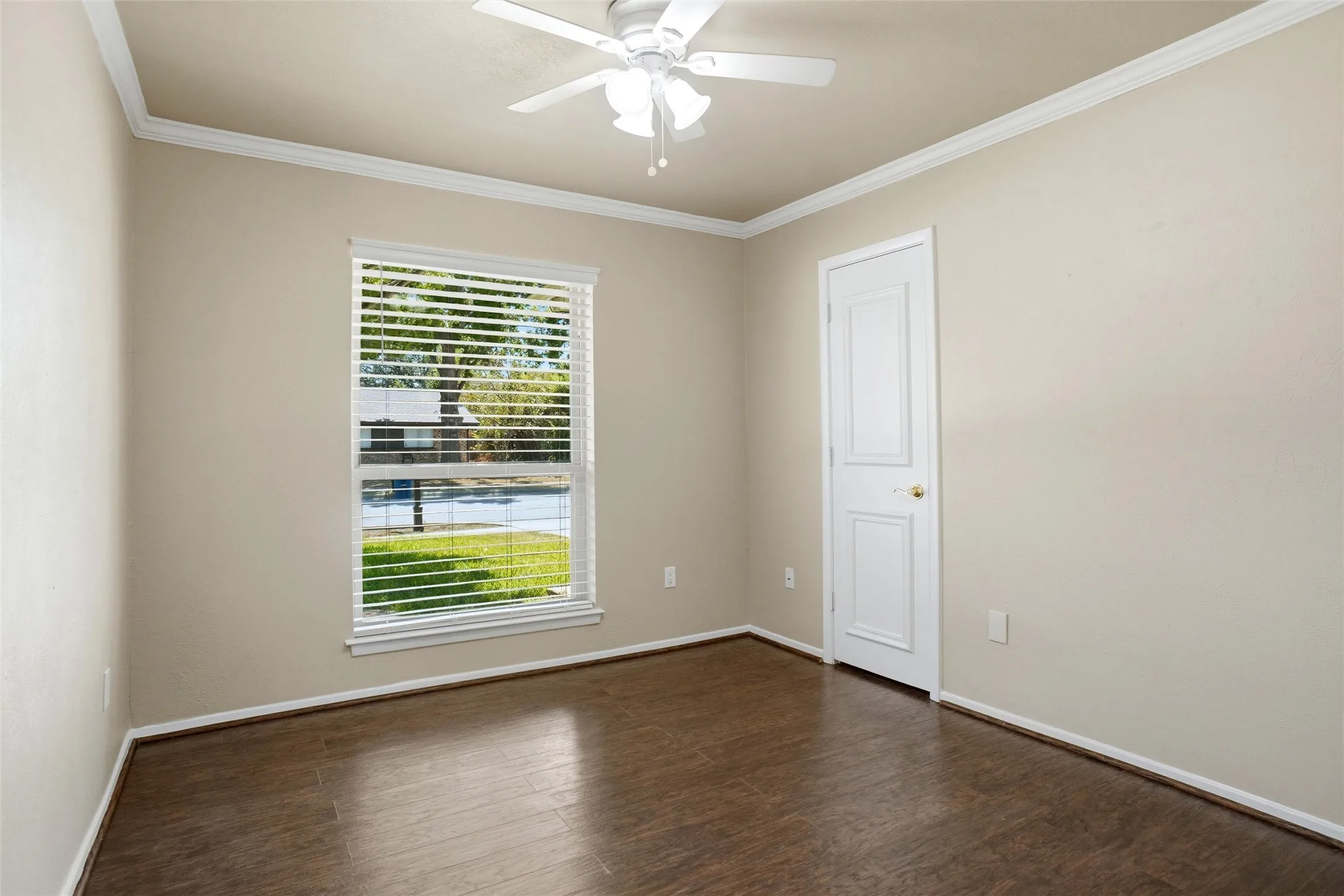 Wood-finish flooring, single window with blinds, ceiling fan, crown molding, and white trim throughout