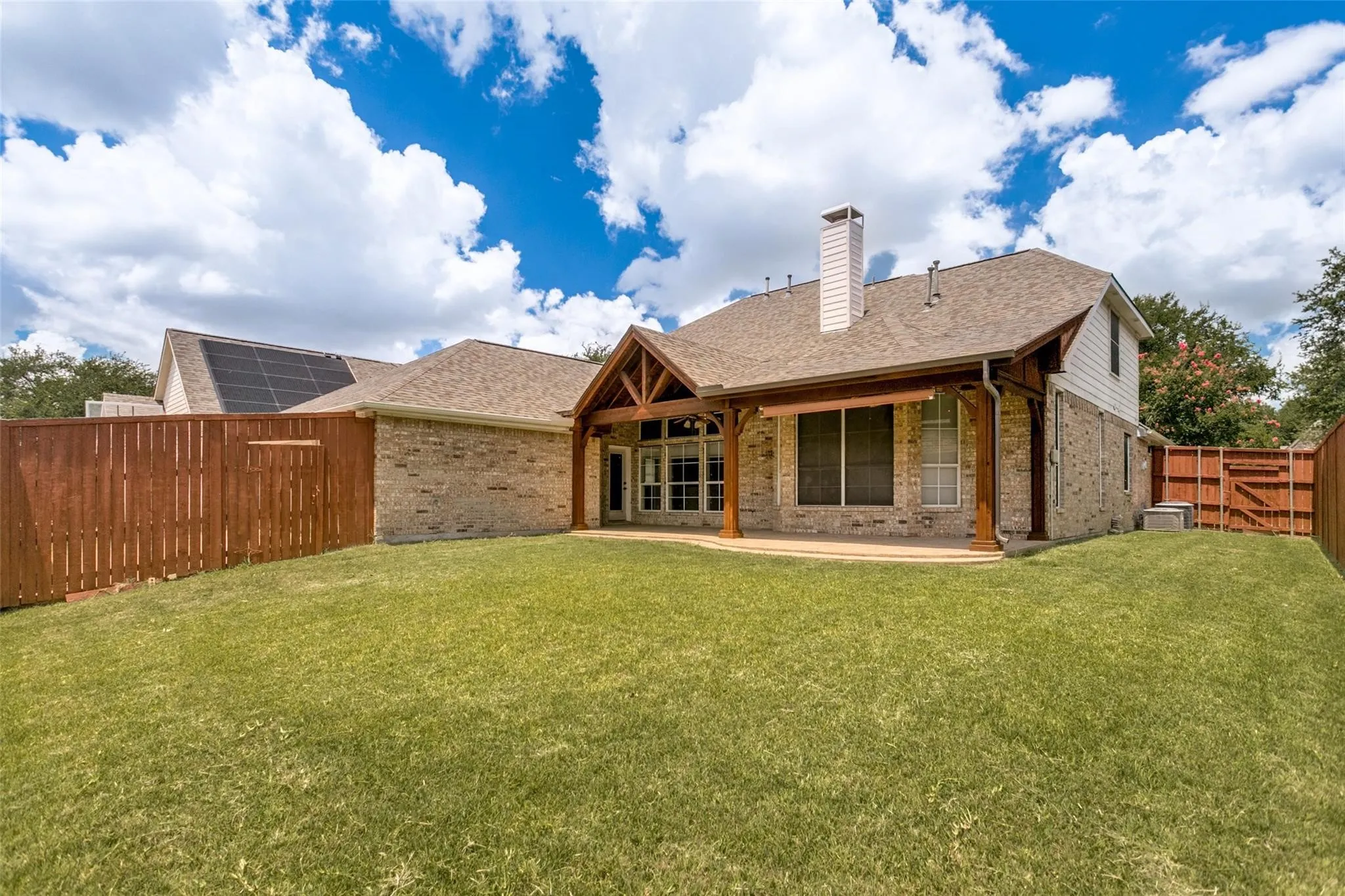 Expansive lawn with a covered patio featuring a wood-beam vaulted ceiling and brick-clad exterior