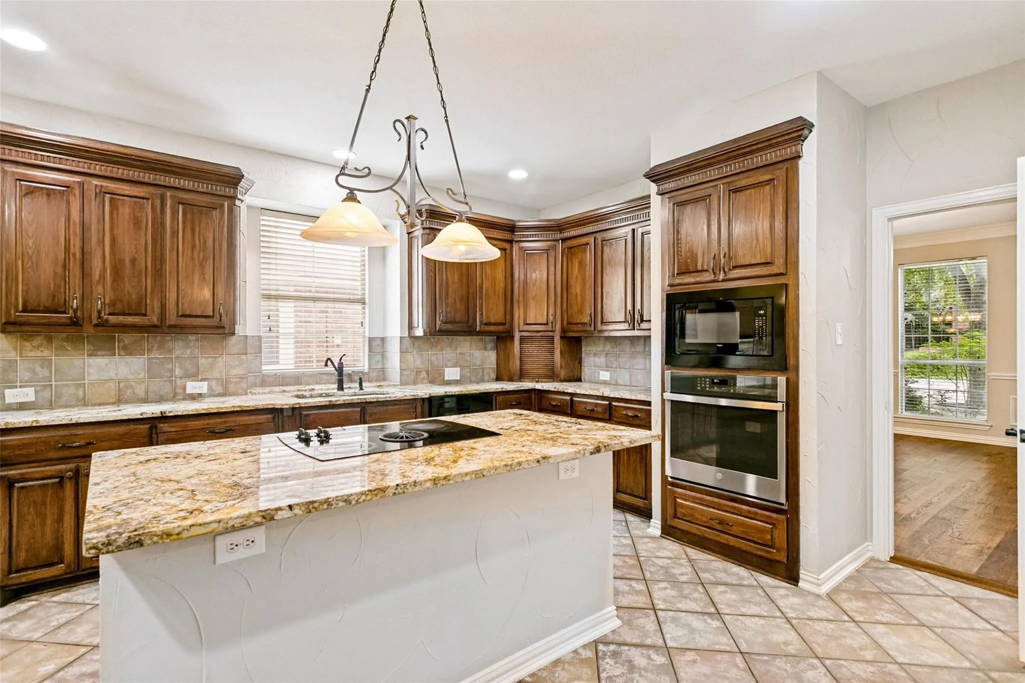 Kitchen featuring rich wood cabinetry, granite countertops, a built-in oven and microwave, an island with an integrated cooktop, and tile flooring