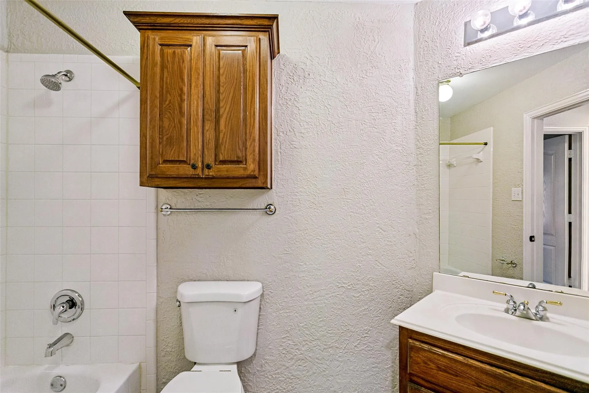 Bathroom featuring a shower-tub combination with white tile surround, wooden wall-mounted cabinetry, a vanity with an integrated sink, and an overhead vanity light fixture
