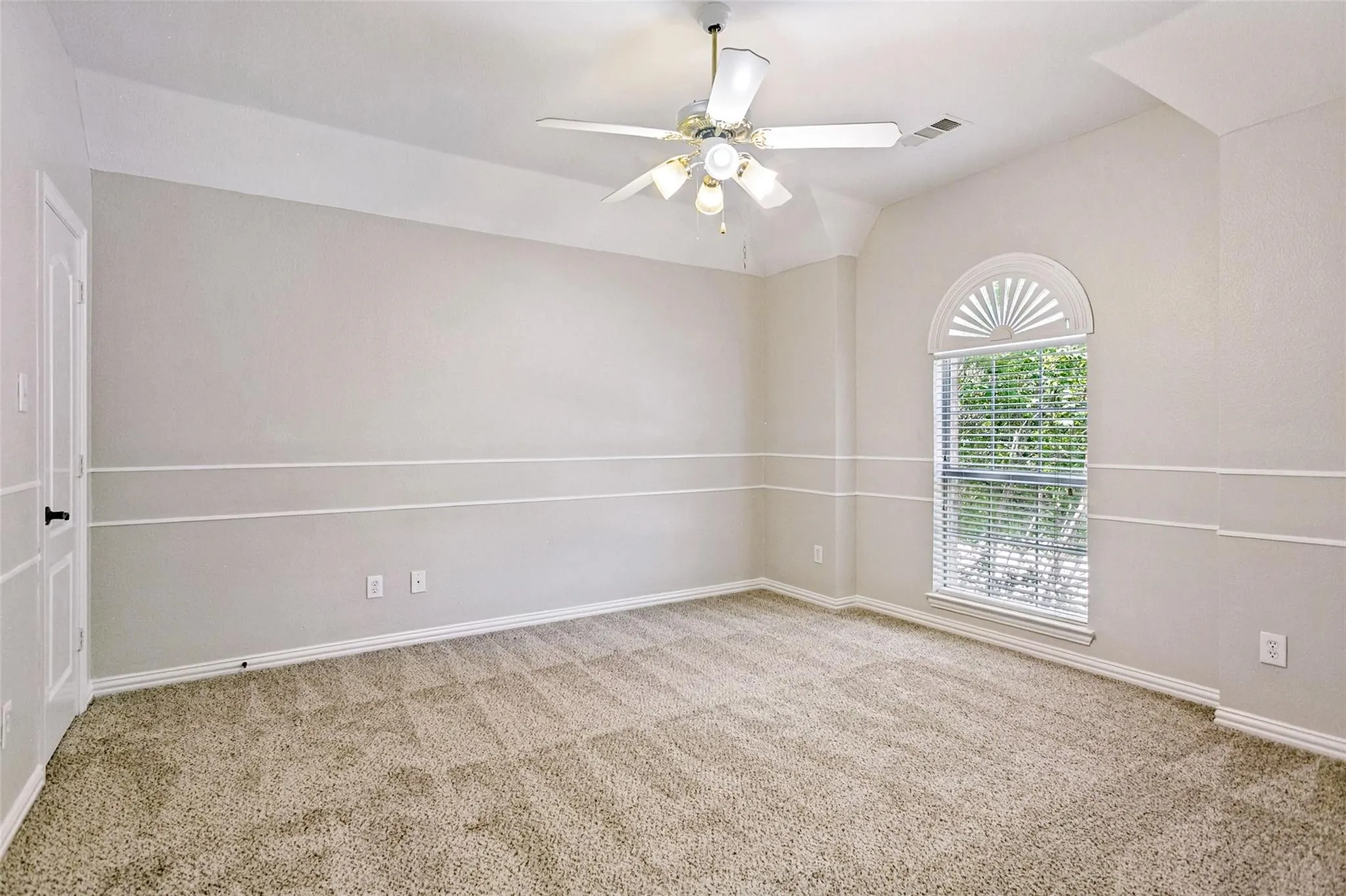 Carpeted room featuring a ceiling fan with light kit, a vaulted ceiling, and an arched window with blinds
