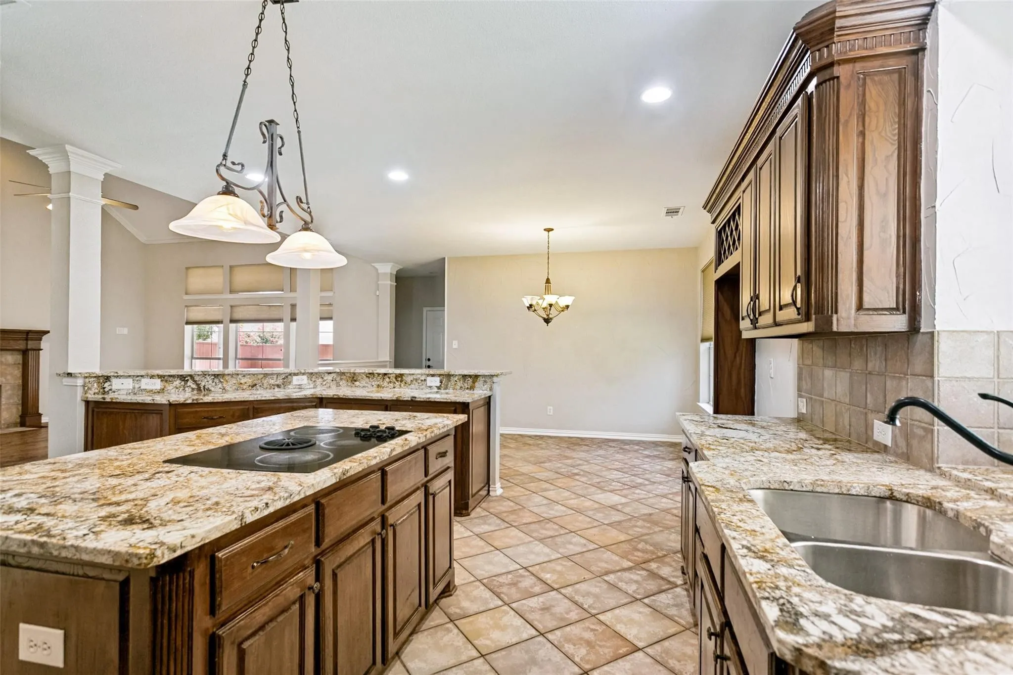 Kitchen featuring a large island with cooktop, double basin sink, stone countertops, and wood-finish cabinetry