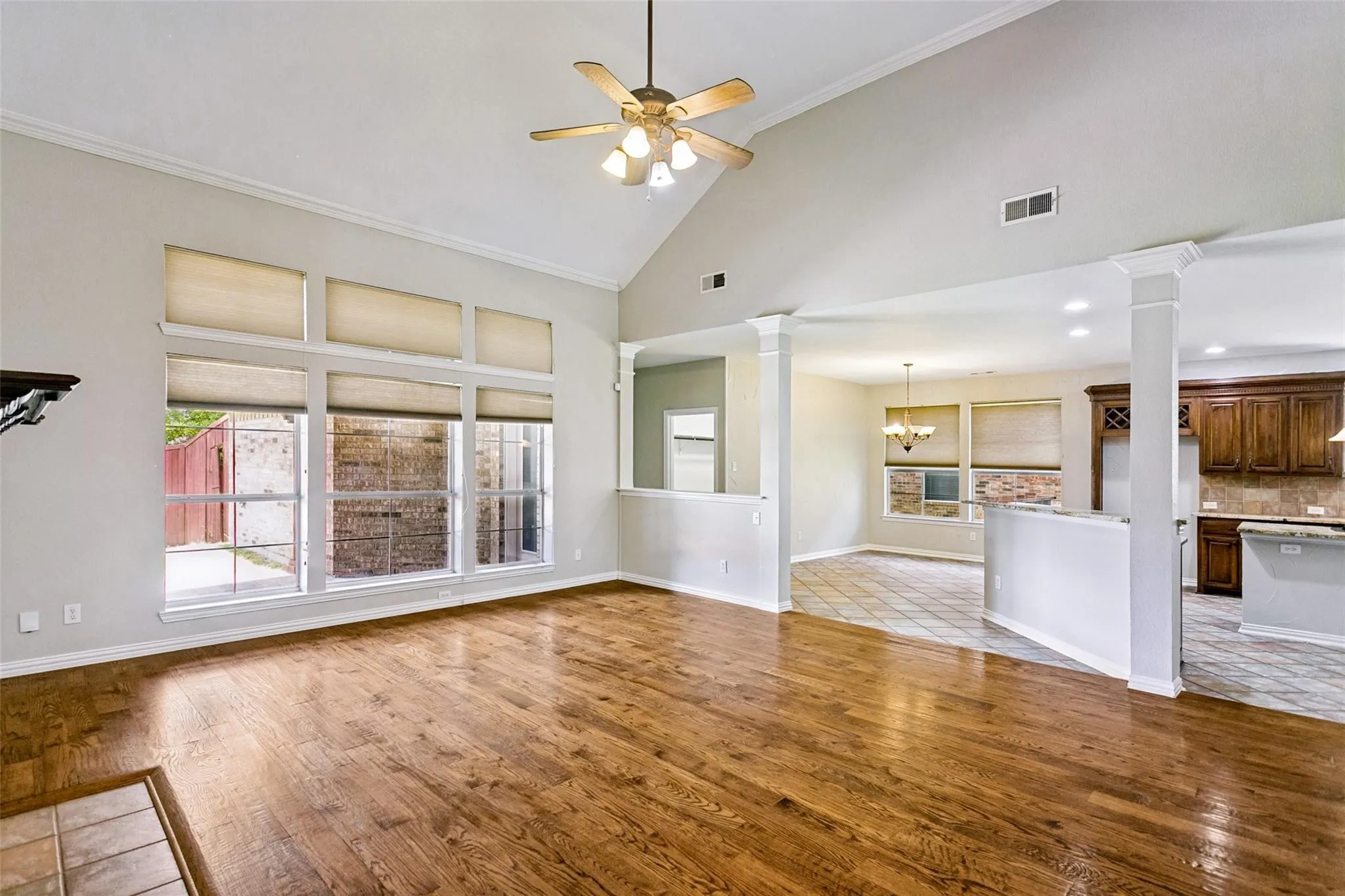 Vaulted ceiling with a ceiling fan, wood-finish flooring, columned half-walls, and large windows