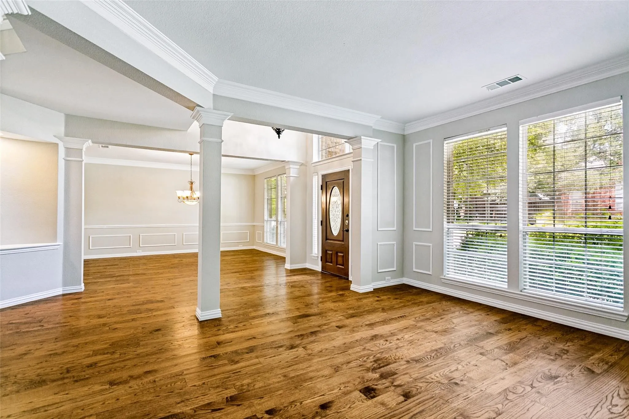 Grand foyer featuring a curved staircase with wrought iron balusters and wood handrails, wood-finish flooring, decorative entryway lighting, and extensive trim work