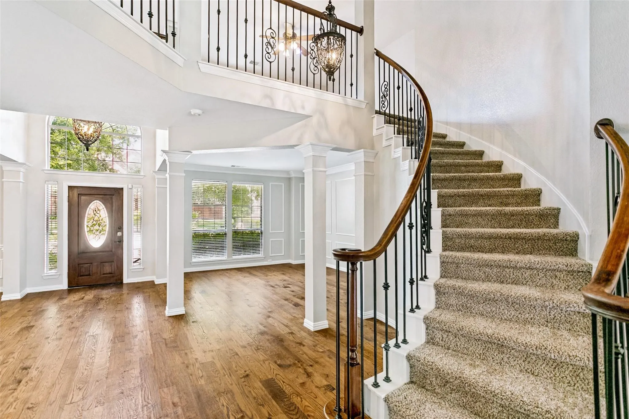 Grand foyer featuring a curved staircase with wrought iron balusters and wood handrails, wood-finish flooring, decorative entryway lighting, and extensive trim work