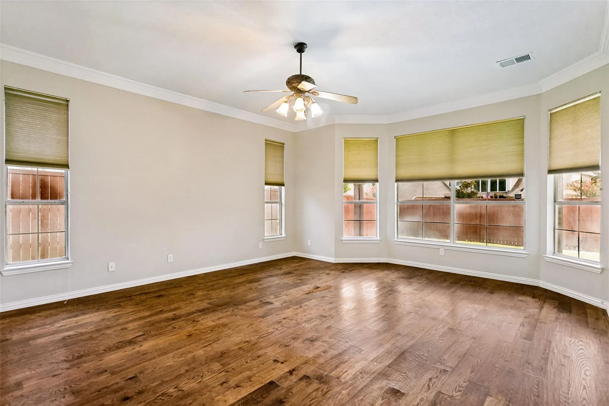Wood-finish flooring, crown molding, ceiling fan, and multiple windows with roller shades