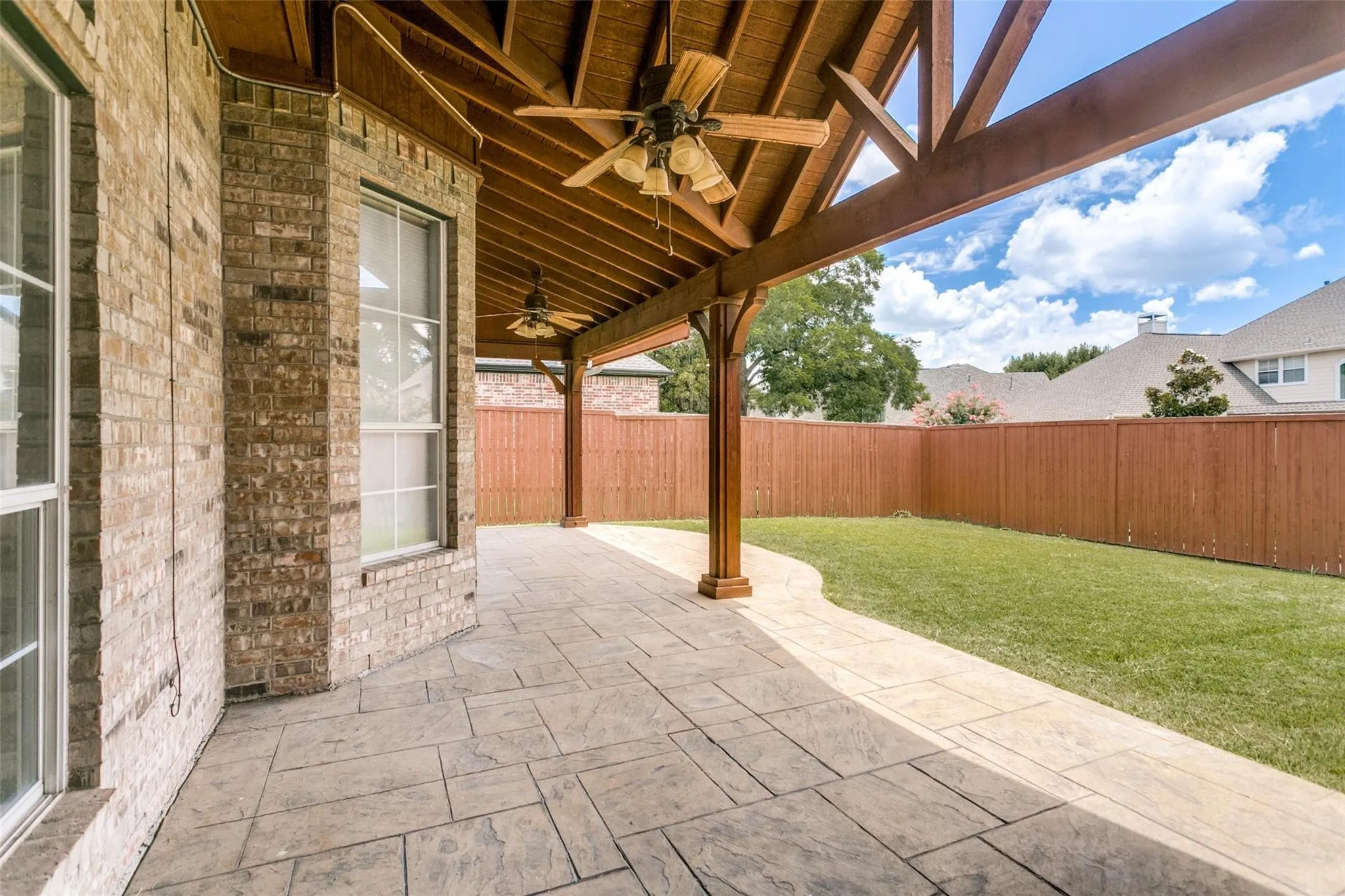 Expansive covered patio with exposed wood beams, dual ceiling fans, and stamped concrete flooring