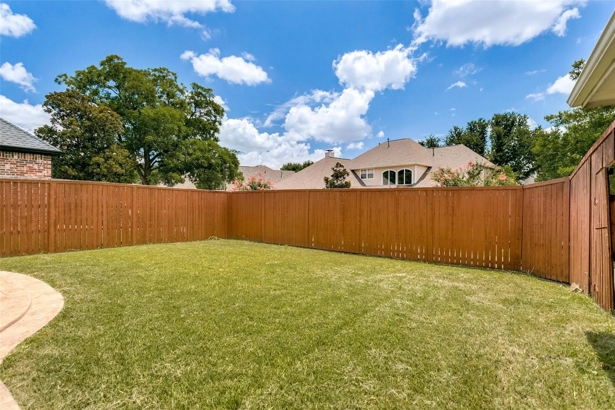 Expansive grassy yard with a curved concrete patio, surrounded by a tall privacy fence