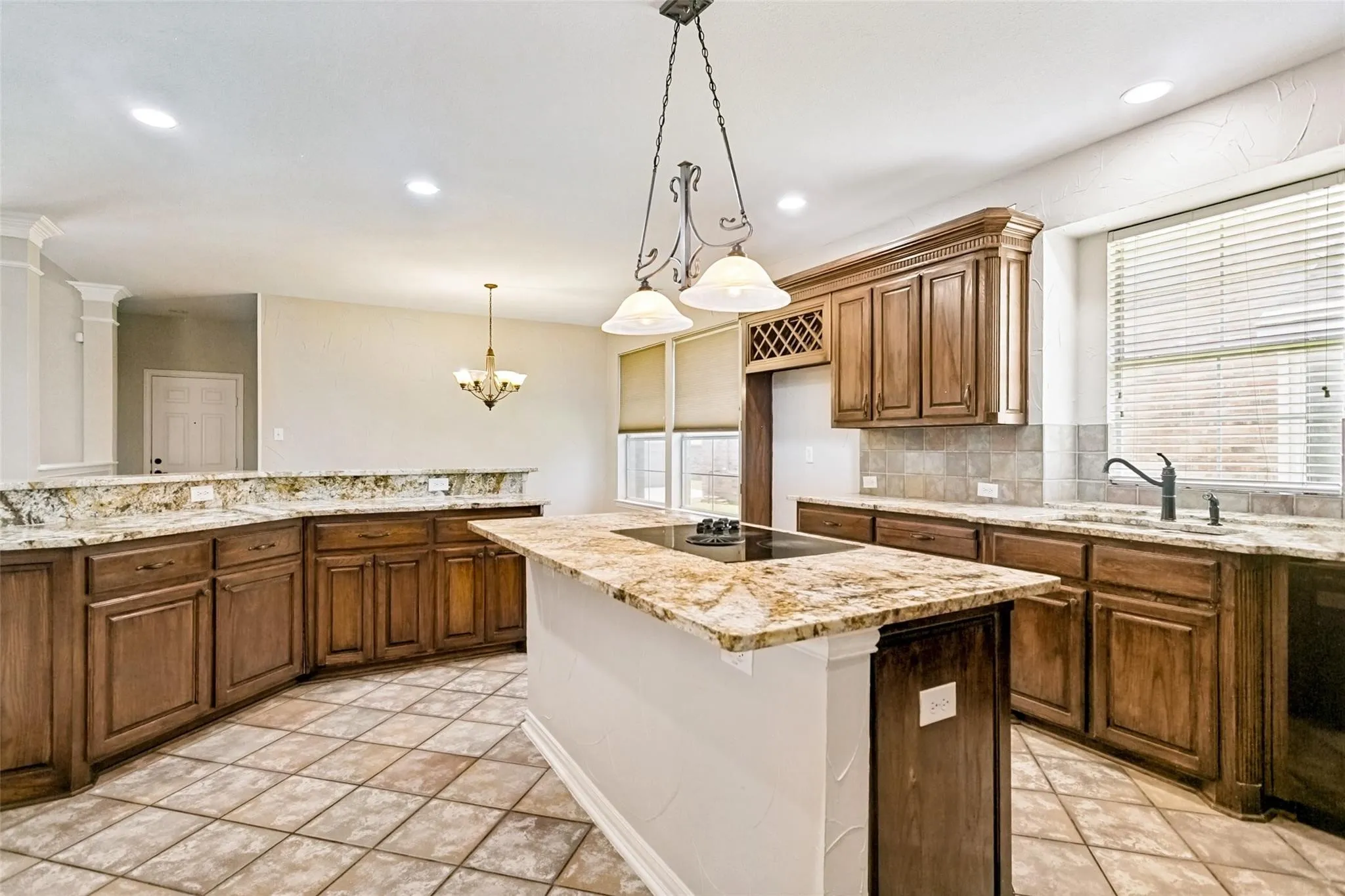 Kitchen featuring an island with a built-in cooktop, granite countertops, wood cabinetry, tile flooring, and a tile backsplash