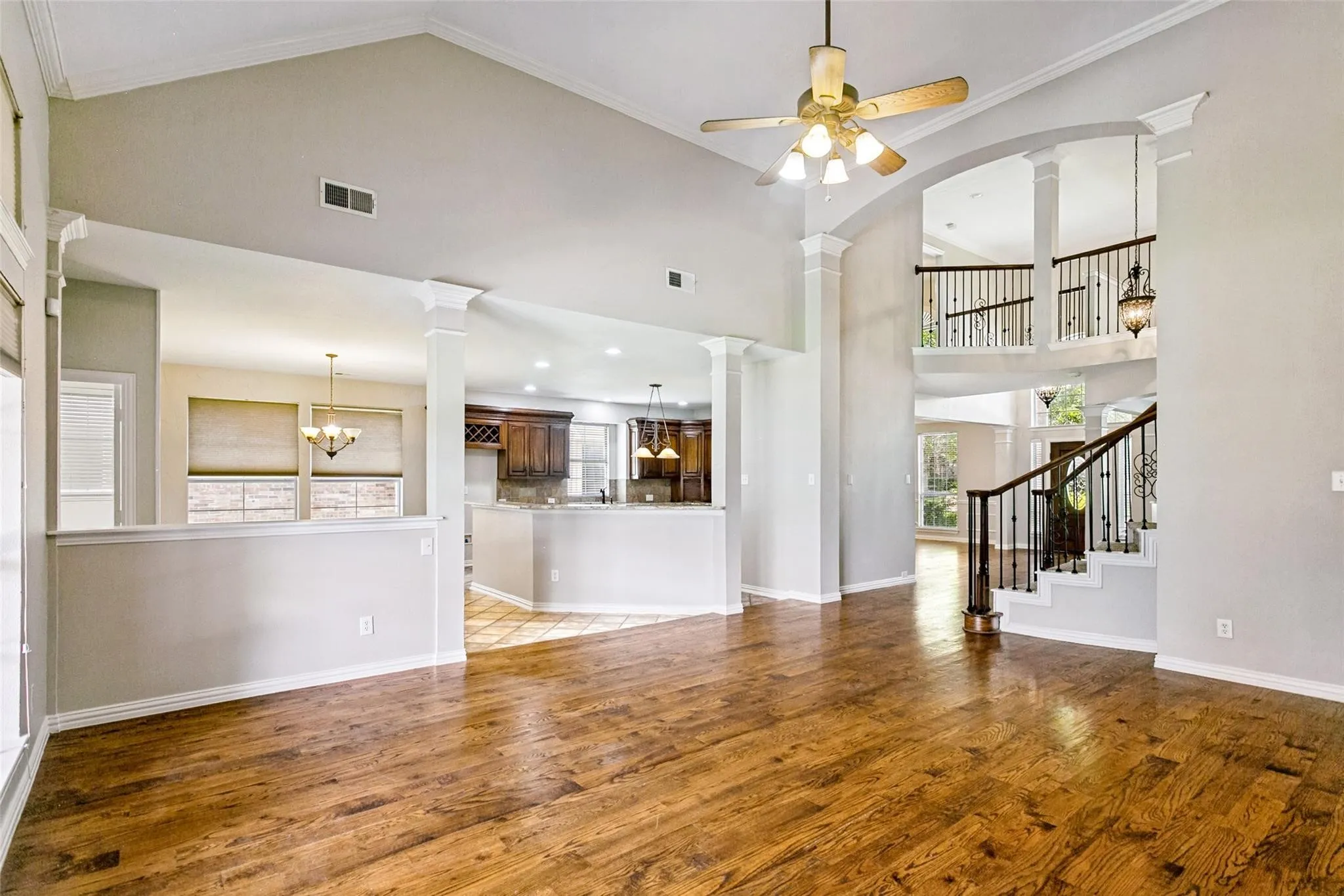 Vaulted ceiling with a ceiling fan light fixture, wood-finish flooring, and a curved staircase with wrought iron balusters