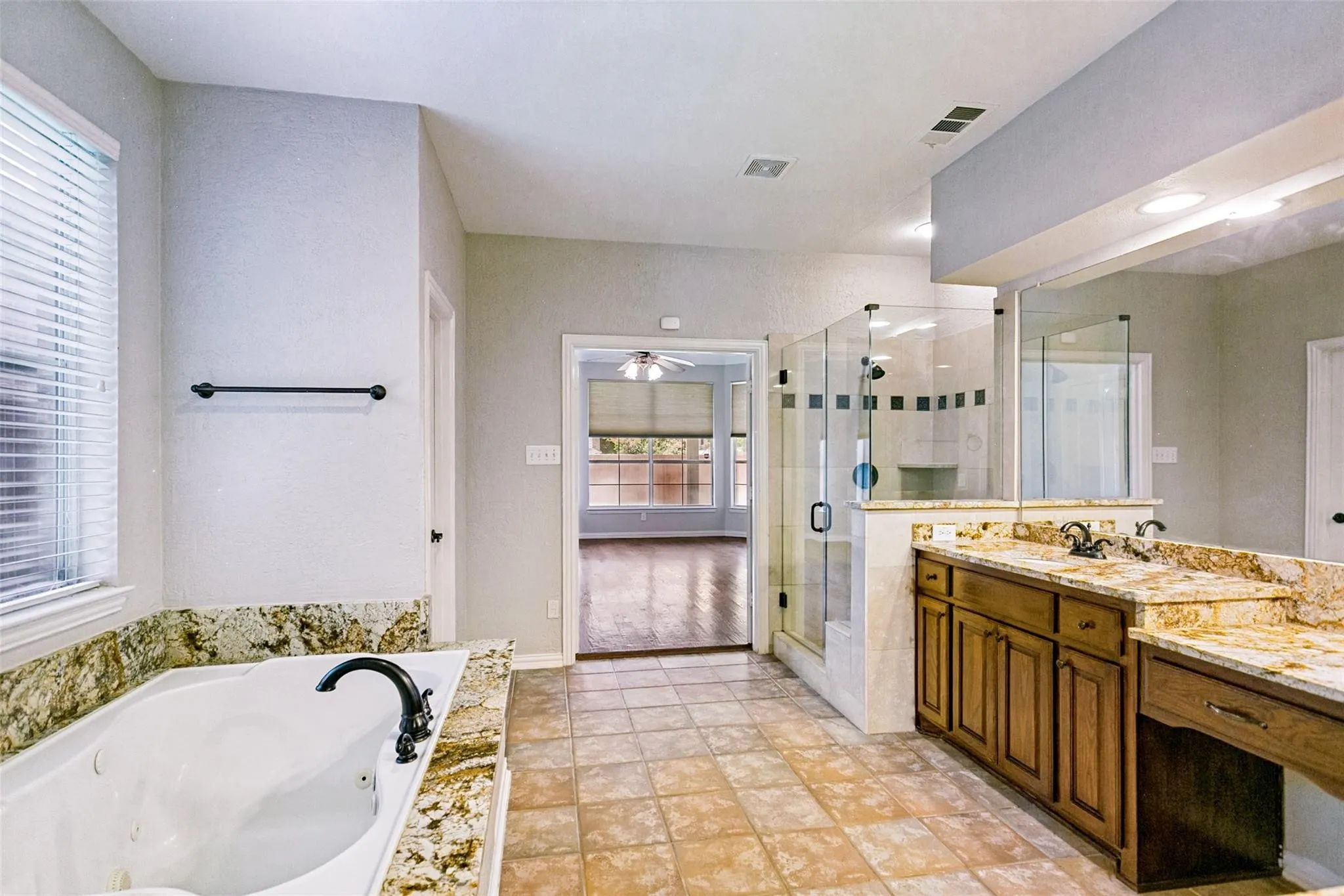 Dual vanity with stone countertops, jetted soaking tub, walk-in shower with glass enclosure, and tiled flooring