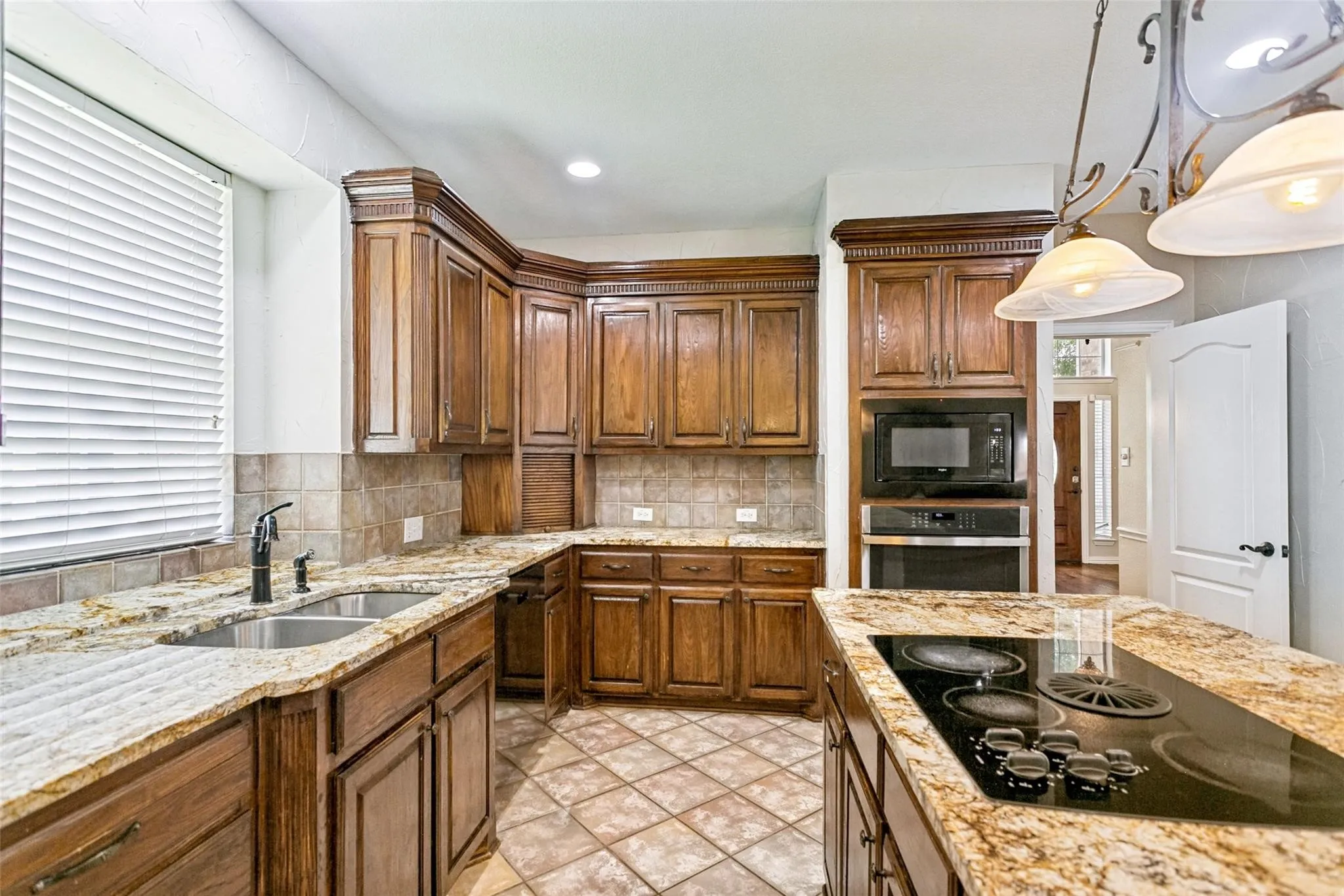 U-shaped kitchen featuring rich wood cabinetry, patterned tile flooring, a large double basin sink with a dark-finish faucet, stone countertops, and a built-in oven with a microwave