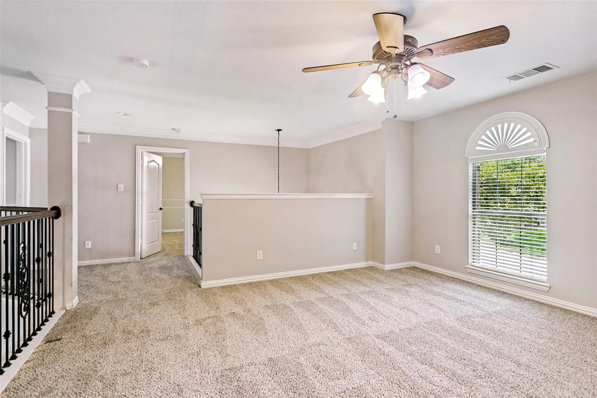 Carpeted loft space with a ceiling fan, decorative arched window, and a wrought iron railing