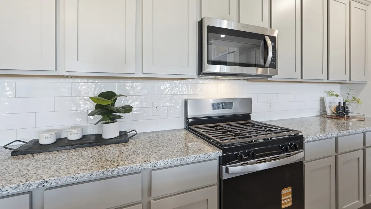 White shaker-style cabinetry with stainless steel hardware, subway tile backsplash, granite-style countertops, and a stainless steel oven and microwave