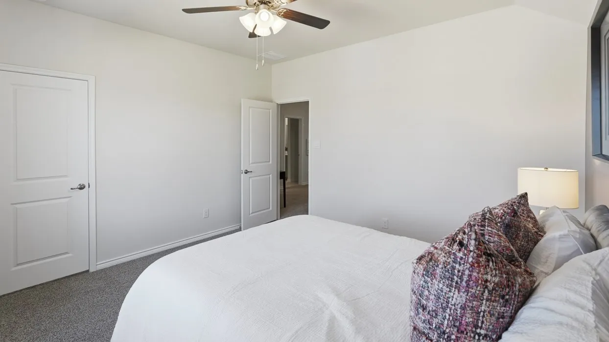 Spacious bedroom featuring neutral wall finishes, carpet flooring, ceiling fan with integrated lighting, and dual closet access