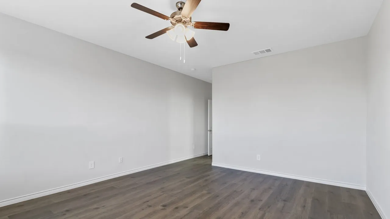 Spacious room featuring wood-finish flooring, light gray walls, and a ceiling fan with light fixture