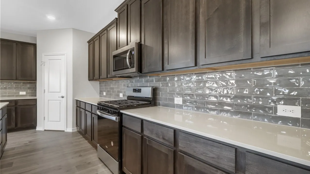 Contemporary kitchen featuring dark wood-finish cabinetry, light-toned countertops, a stainless steel gas range, and a coordinating microwave