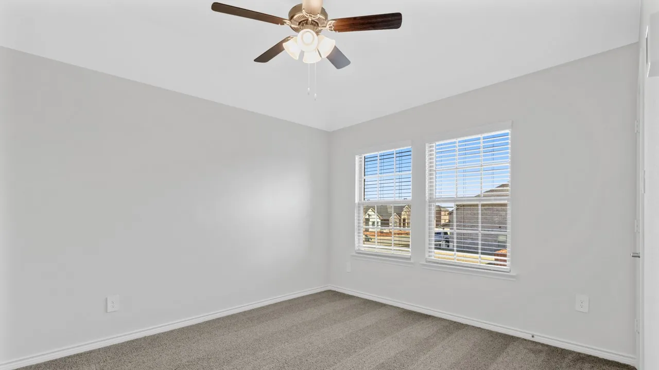 Room with neutral-toned walls, gray carpet, a ceiling fan with light, and two windows