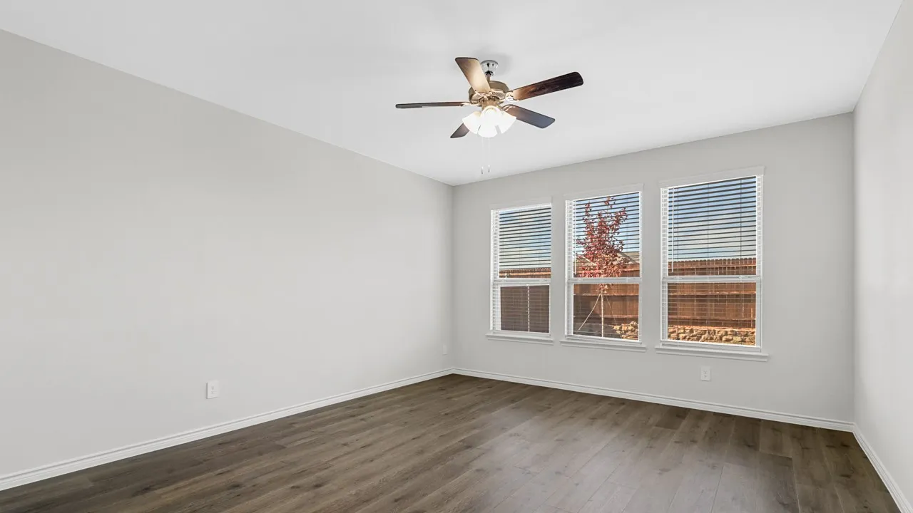 Light gray walls, wood-finish flooring, ceiling fan with integrated lighting, three windows with blinds
