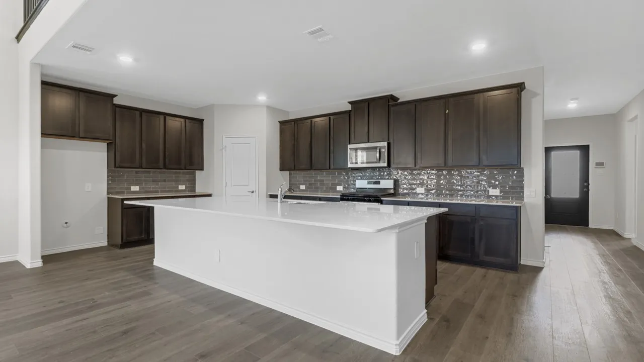 Spacious kitchen featuring an expansive central island, dark wood-finish cabinetry, a textured tile backsplash, and wood-finish flooring
