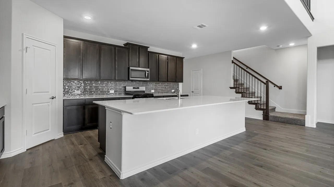 Kitchen featuring a large island with a light-toned countertop, dark wood-finish cabinetry, stainless steel appliances, and a mosaic tile backsplash
