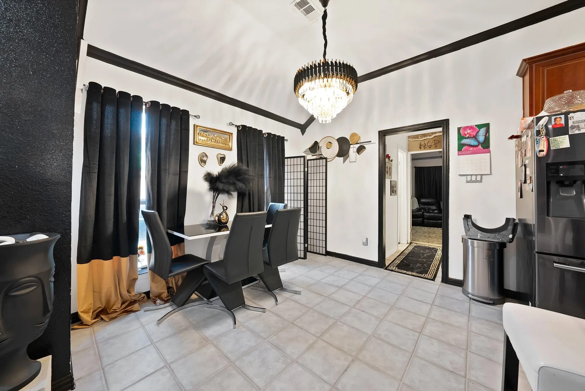 Vaulted ceiling featuring a tiered chandelier, tile flooring, and a stainless steel refrigerator