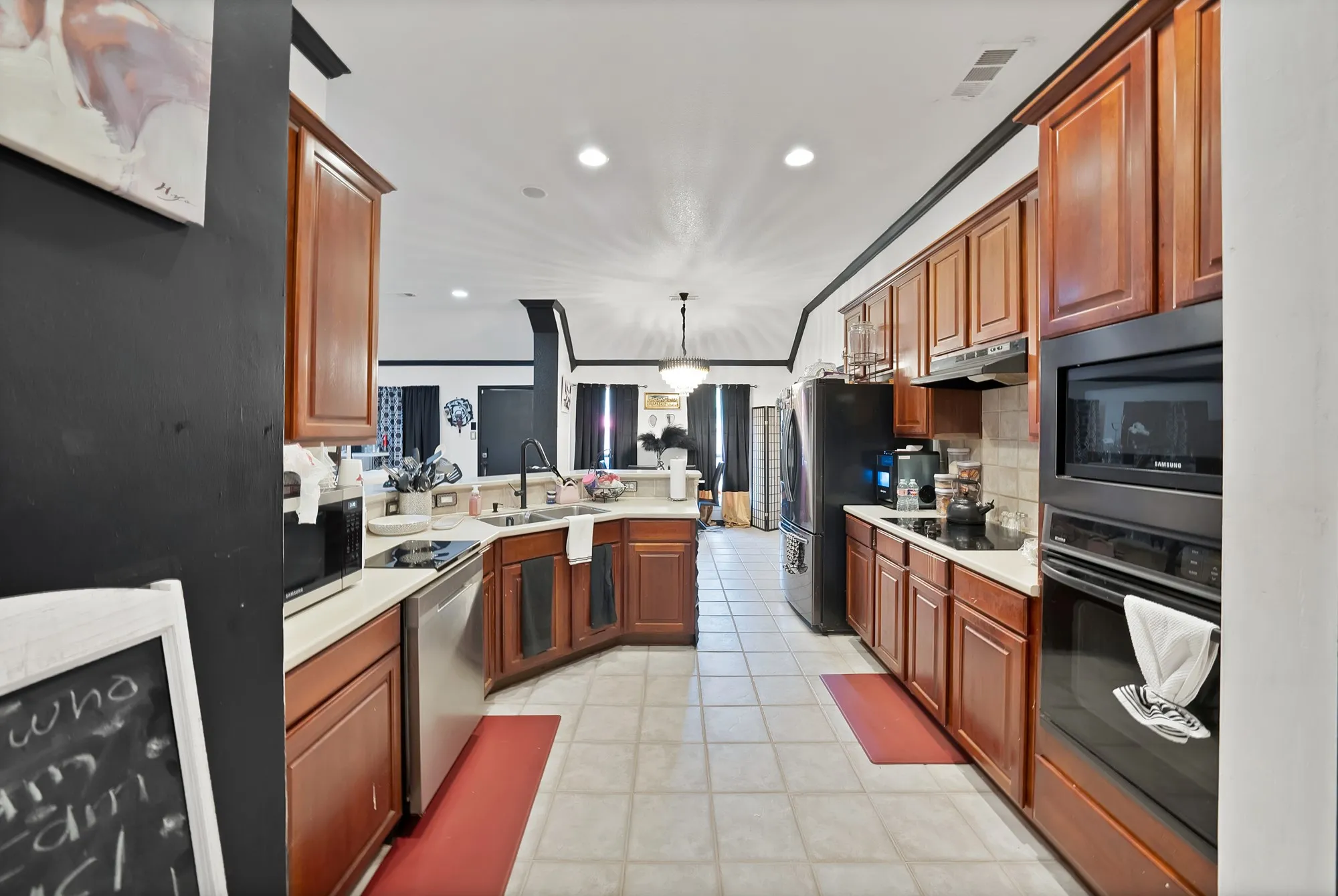 Kitchen featuring wood cabinetry, light countertops, integrated wall oven and microwave, stainless steel dishwasher, and tile flooring