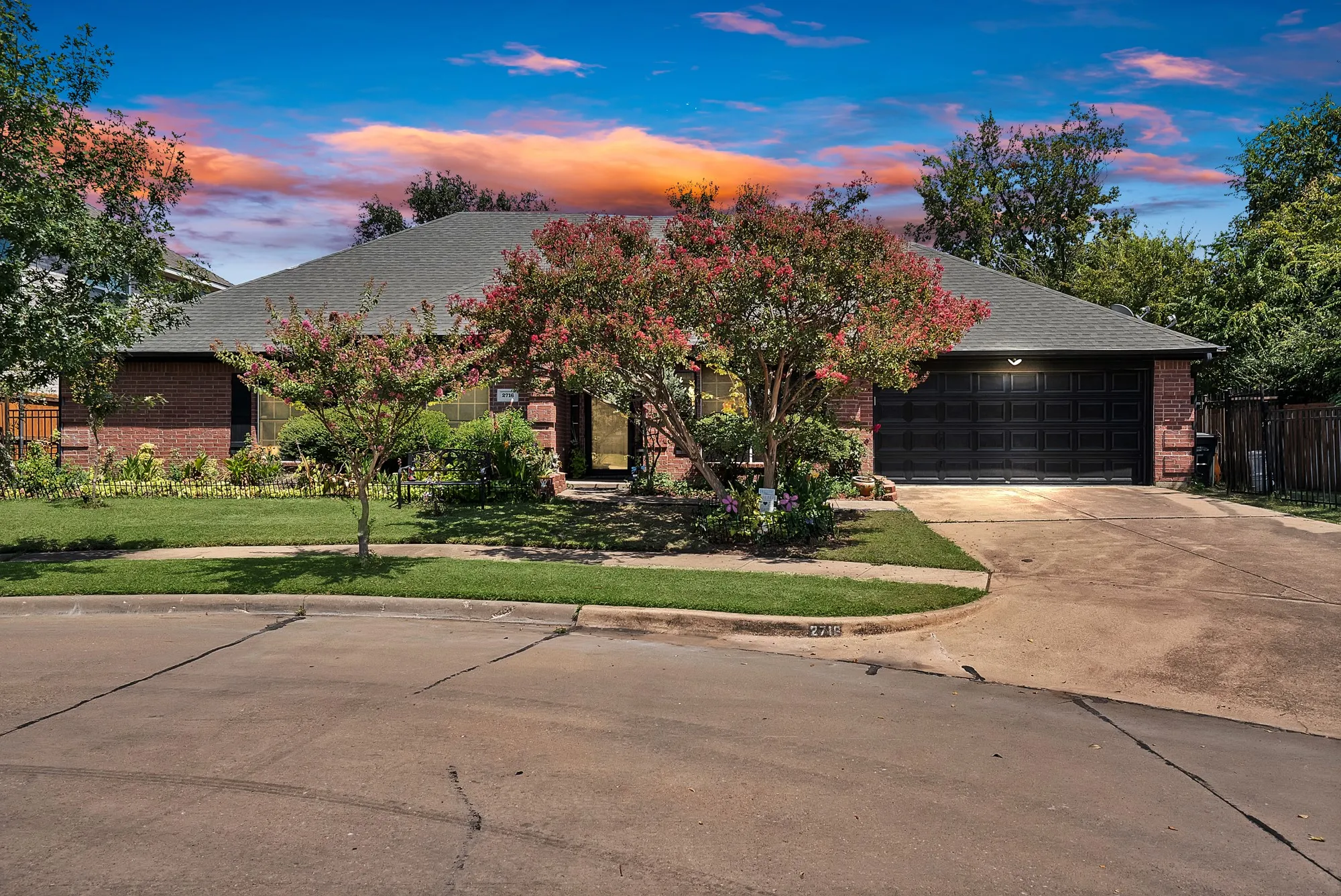 Brick exterior, attached garage, paved driveway, mature landscaping, and a manicured lawn