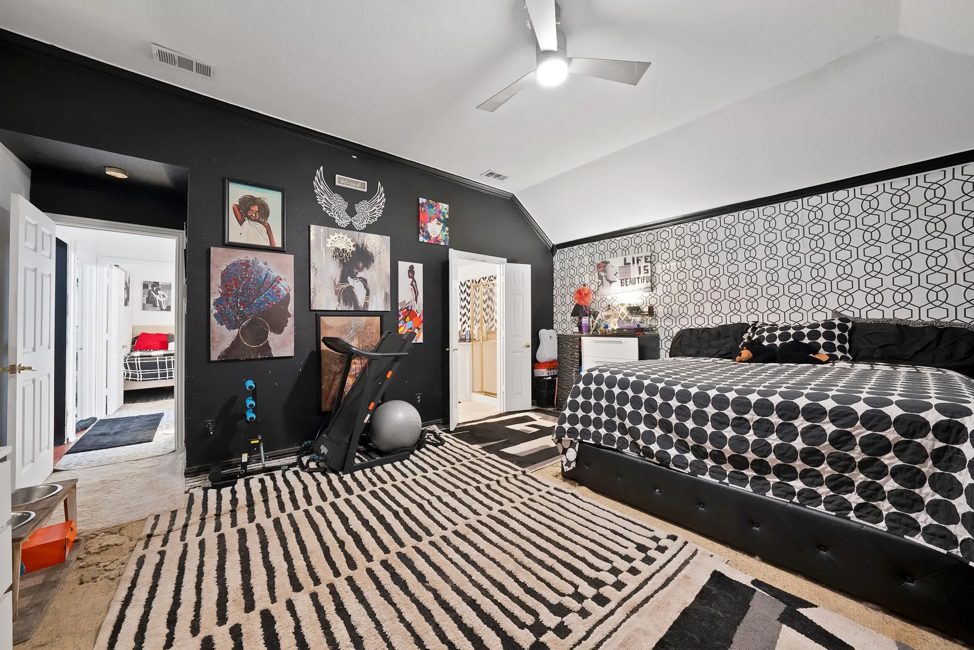 Vaulted ceiling with a ceiling fan, black accent wall, and patterned wallpaper