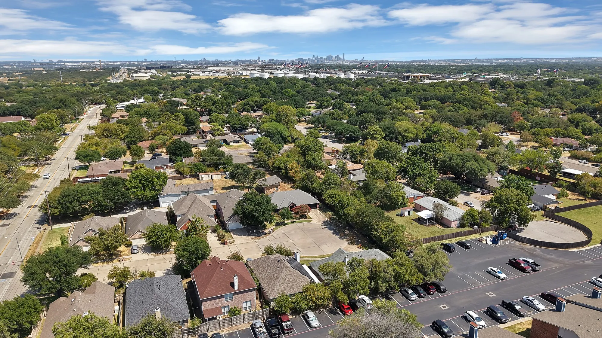 Residential neighborhood featuring mature trees, paved streets, and a distant city skyline