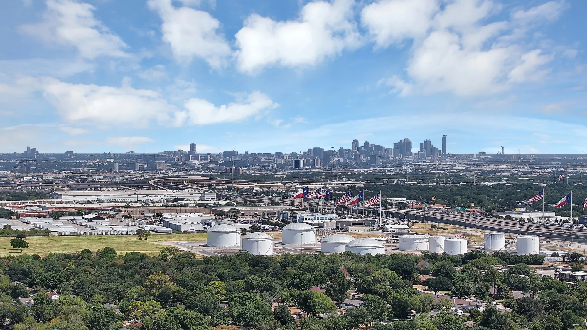Expansive urban skyline with diverse architectural structures, highway infrastructure, and significant green spaces