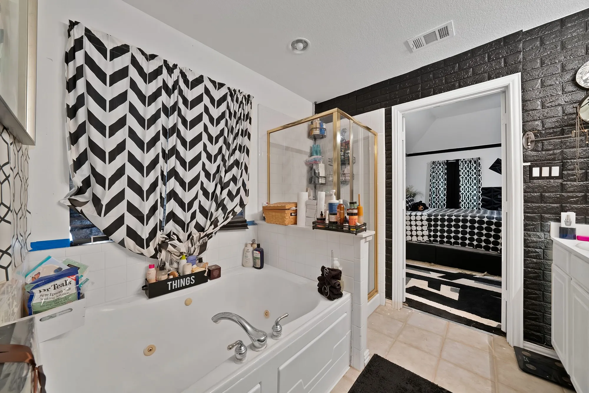 Soaking tub with jetted features, separate shower enclosure with gold-tone framing, white vanity with integrated sink, and dark textured wall covering
