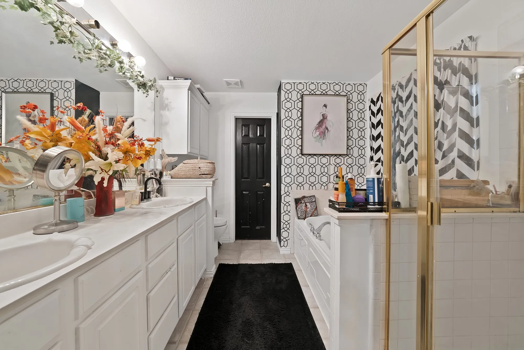 Dual vanity with white cabinetry, built-in bathtub, and an enclosed shower with gold-finish framing