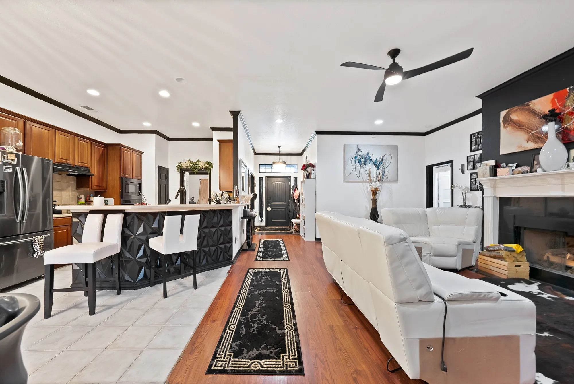 Open-concept living space featuring wood-finish flooring, a kitchen island with seating, a built-in fireplace, and a ceiling fan