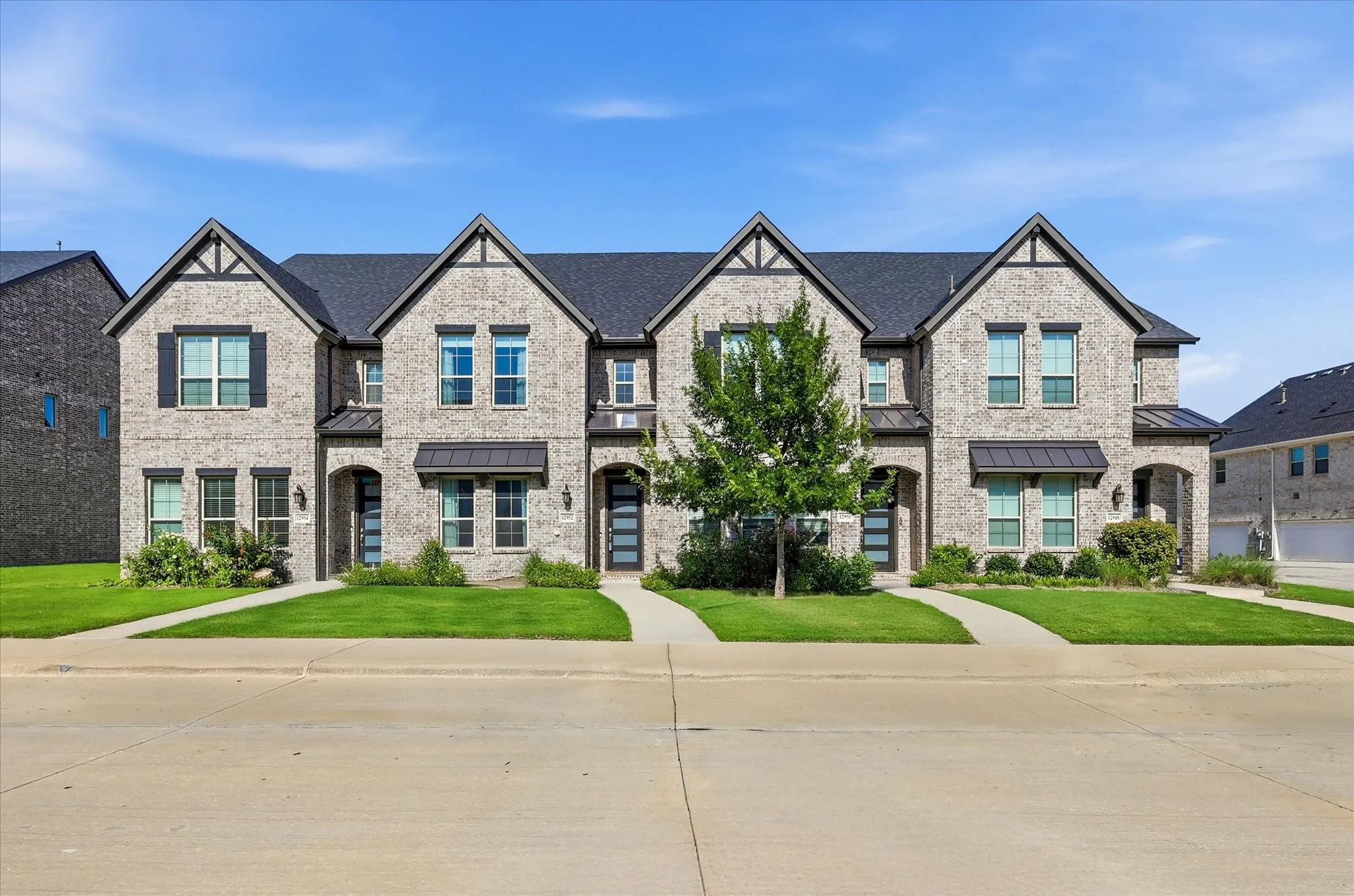 Modern townhome featuring light gray brick exterior, dark gabled rooflines, black window shutters and contemporary entry doors with frosted glass panels.