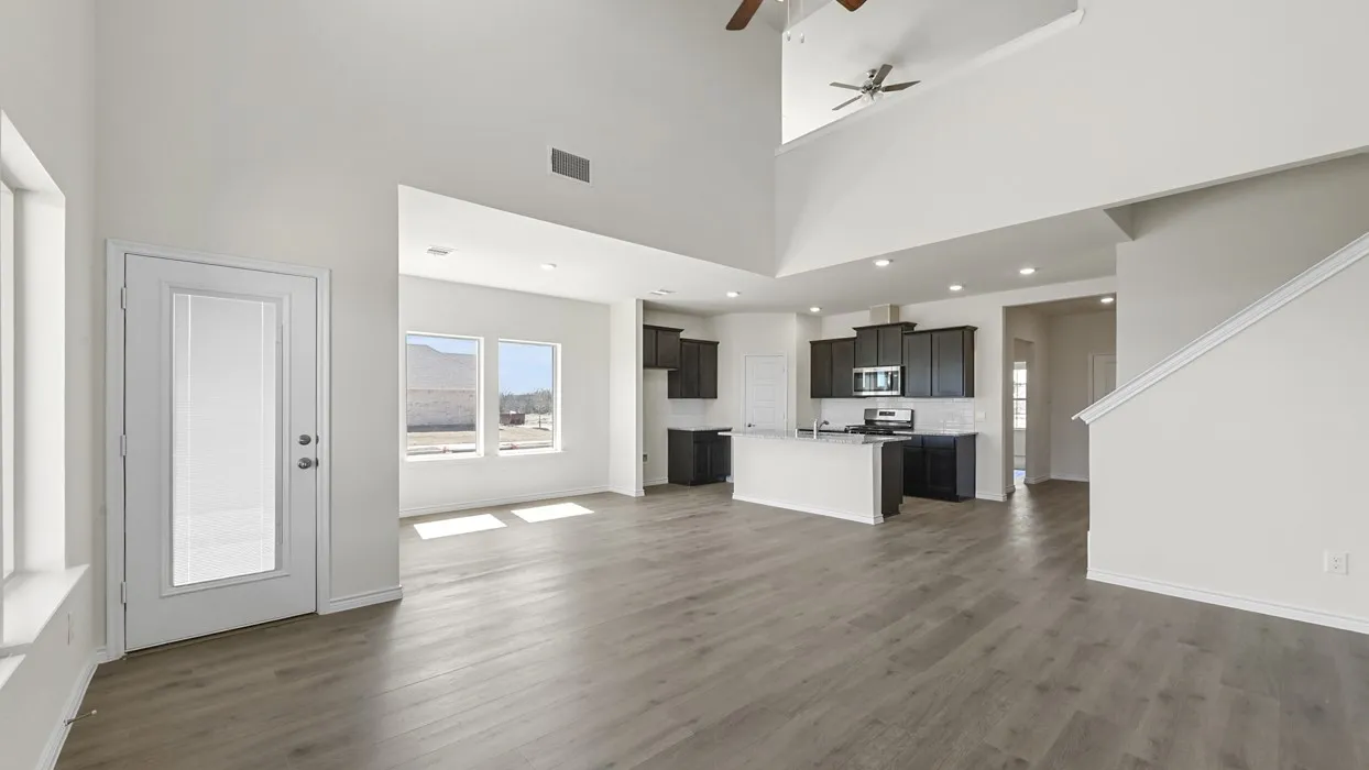 Open-concept layout with high ceilings, wood-finish flooring, recessed lighting, a modern kitchen with dark cabinetry, and multiple windows providing ample natural light
