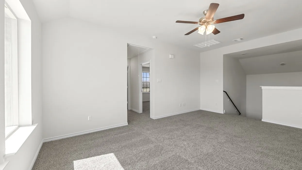 Carpeted open area featuring a ceiling fan, multiple windows, and a staircase