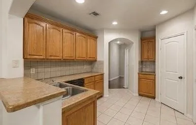Kitchen featuring wood cabinetry, a double basin stainless steel sink, tiled backsplash, and recessed lighting