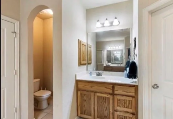 Bathroom featuring a wood-finish vanity with a built-in sink, a large wall-mounted mirror, and overhead vanity lighting