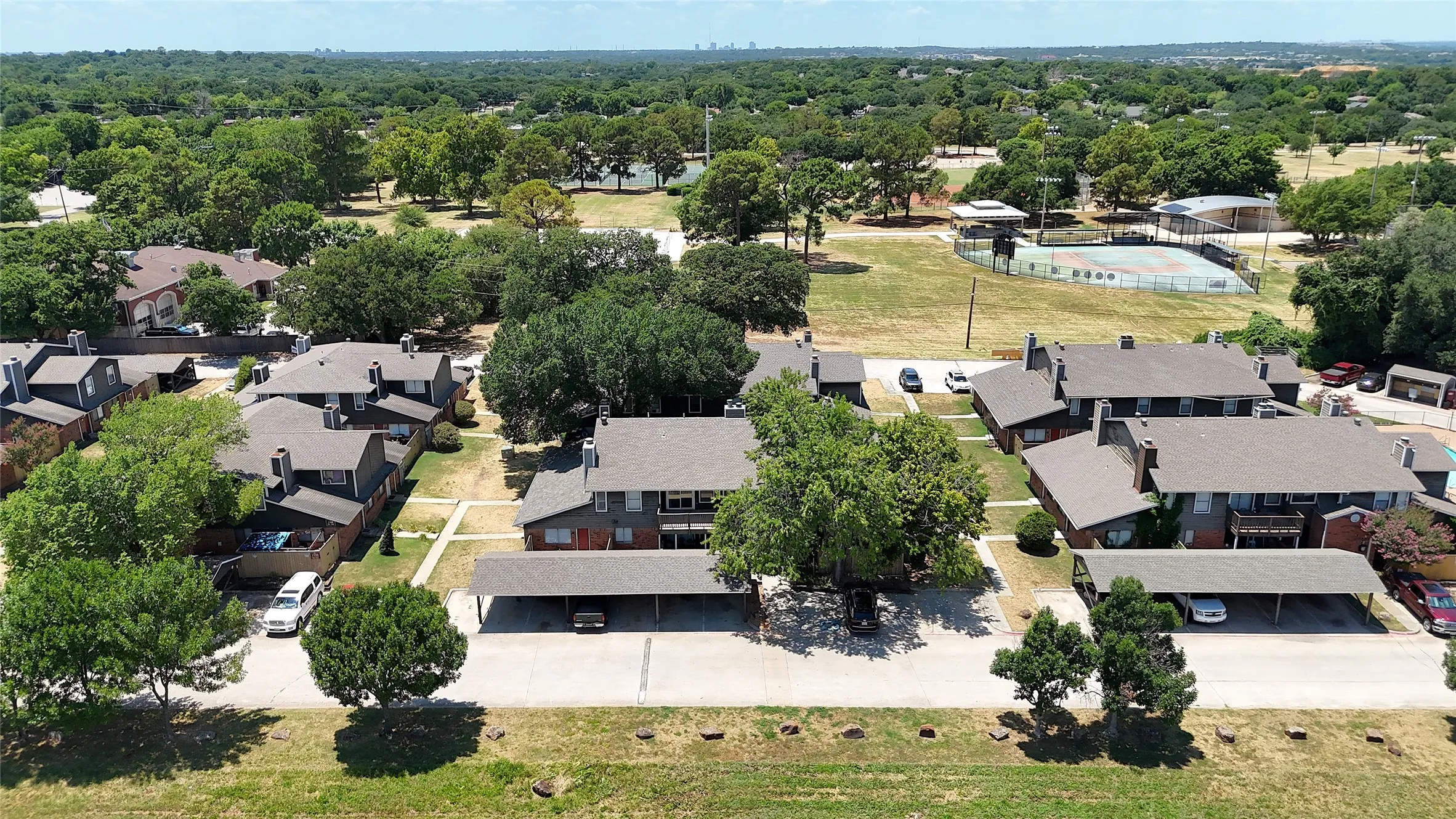 Multiple residential buildings with gabled roofs, a partial tennis court, and covered parking structures