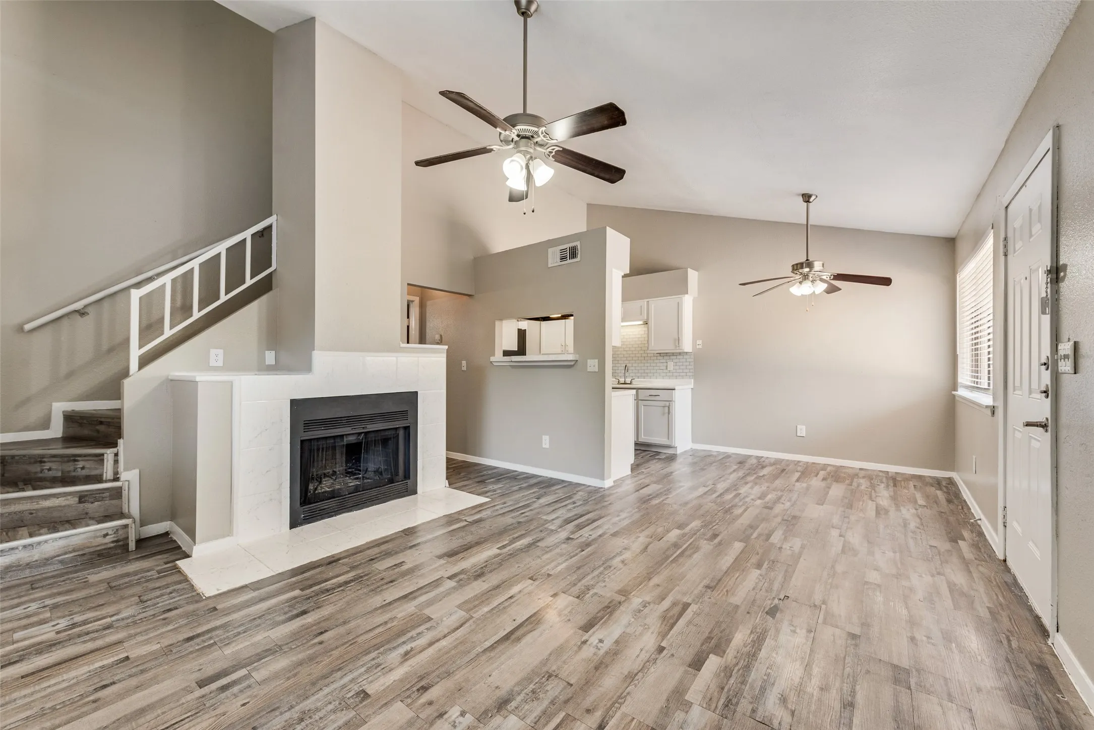 Open-concept living area with wood-finish flooring, a tiled fireplace, and vaulted ceilings