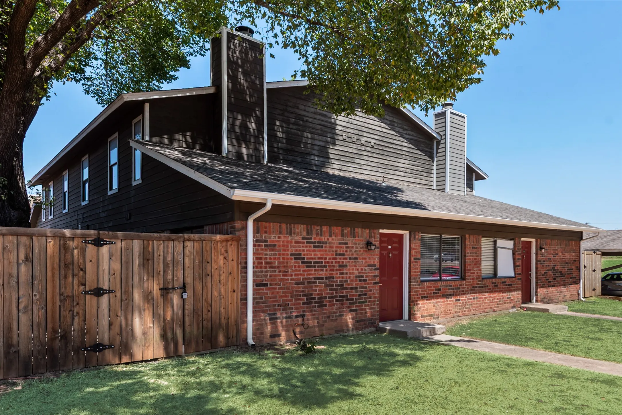 Brick exterior with wood siding, dual red entry doors, and a wood privacy fence