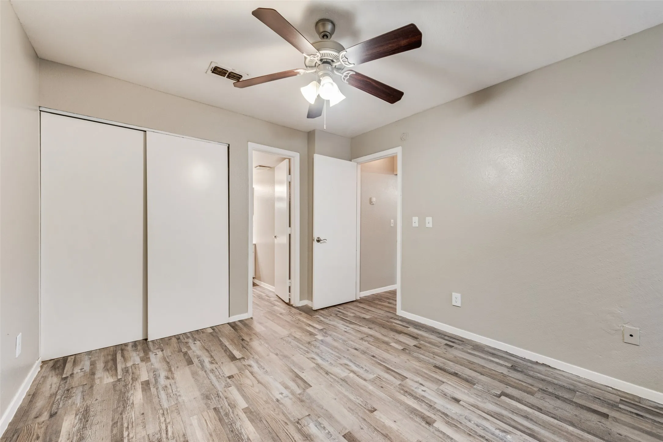 Wood-finish flooring throughout, ceiling fan with light fixture, and sliding closet doors