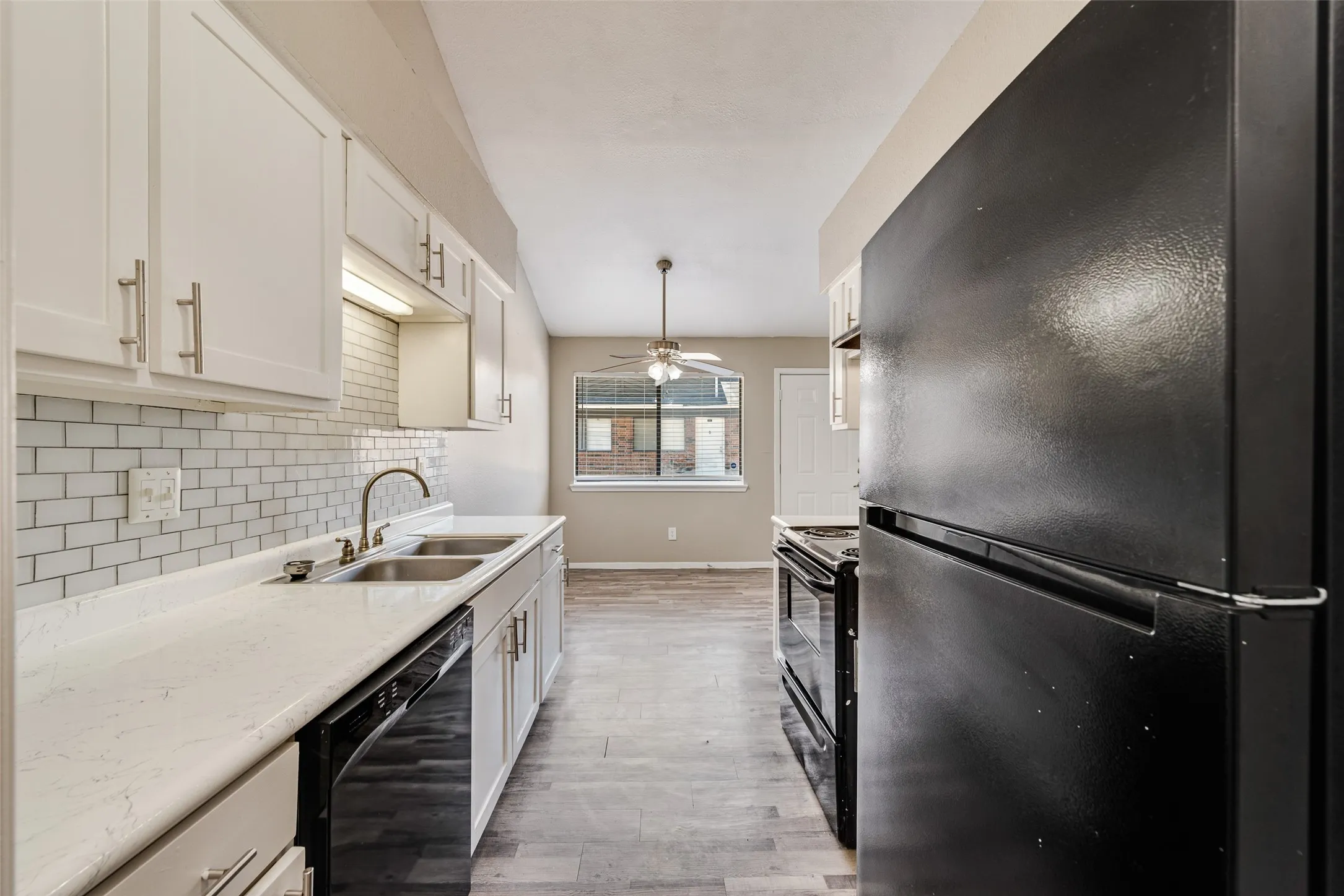 Modern galley kitchen featuring white shaker cabinetry with brushed nickel hardware, subway tile backsplash, stainless steel appliances including a double wall oven, black finish gas range, and refrigerator with ice maker, quartz countertops, and wood-finish flooring throughout