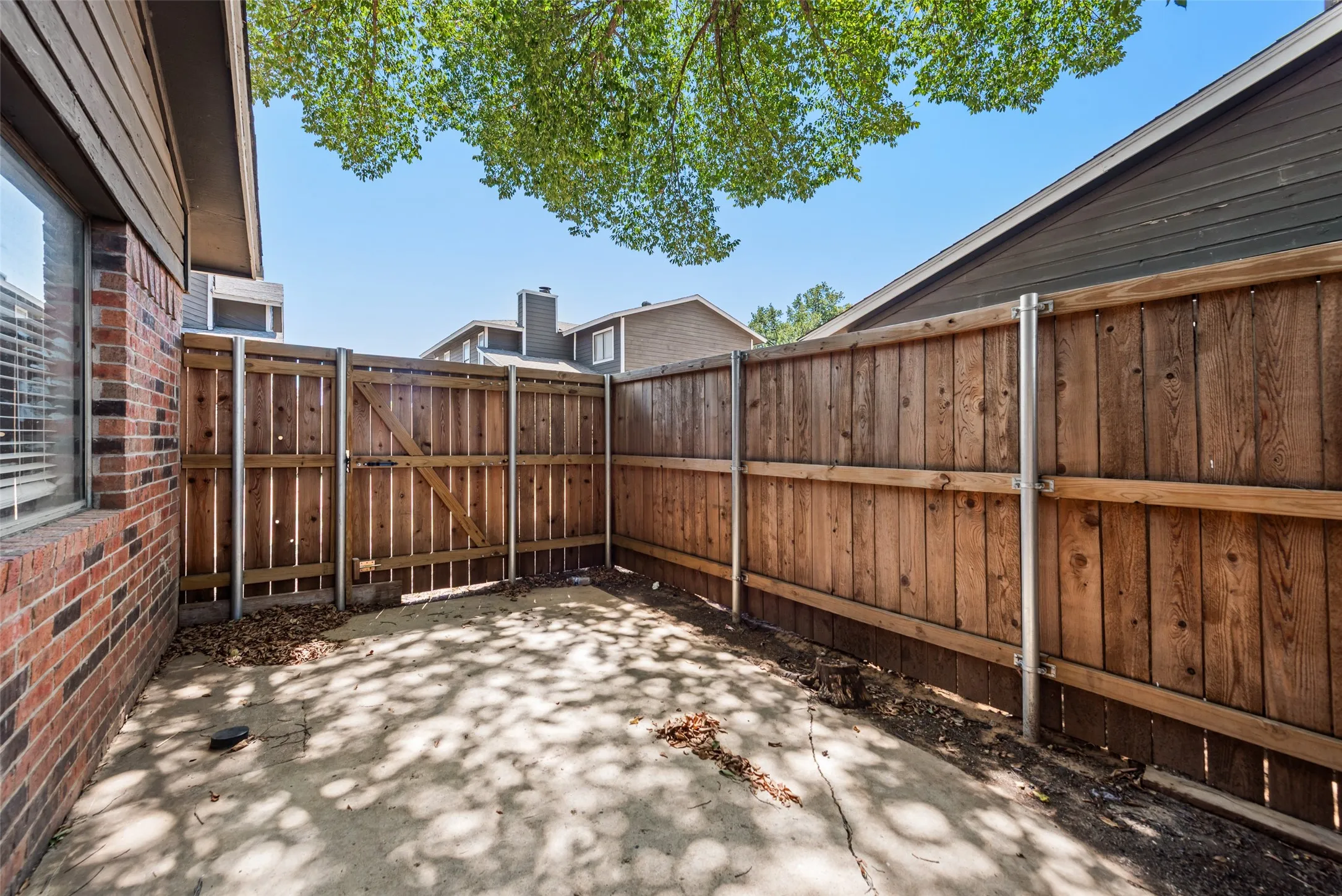 Concrete patio with wood fencing, a secure gate, and brick exterior