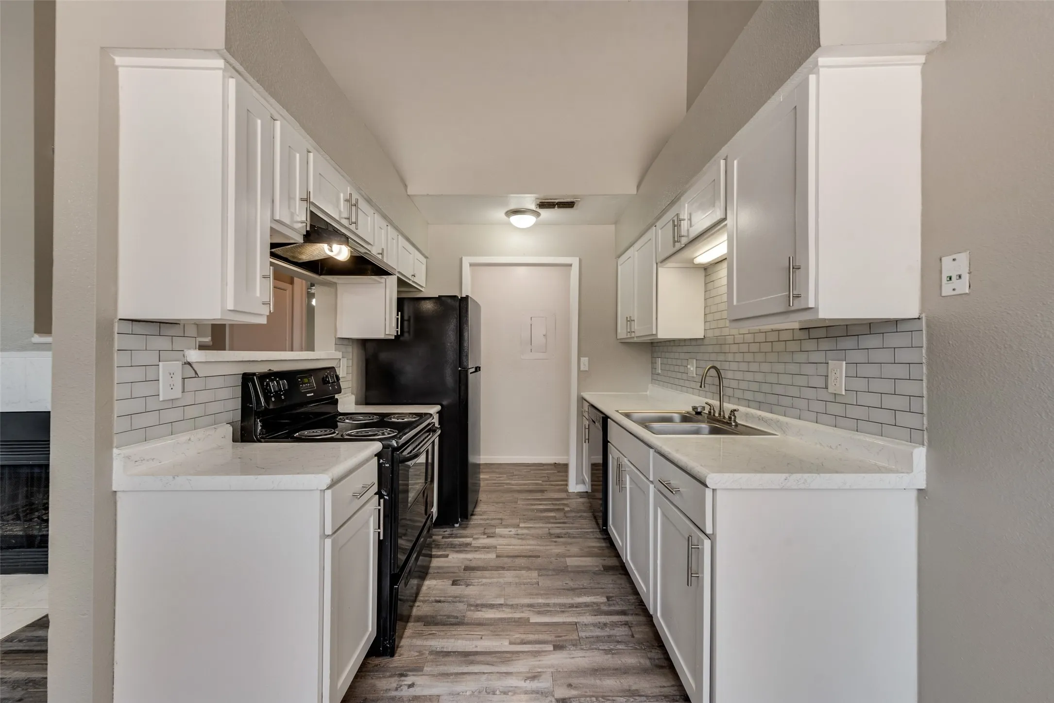 Galley kitchen featuring white cabinetry, light countertops, subway tile backsplash, black appliances, and wood-finish flooring