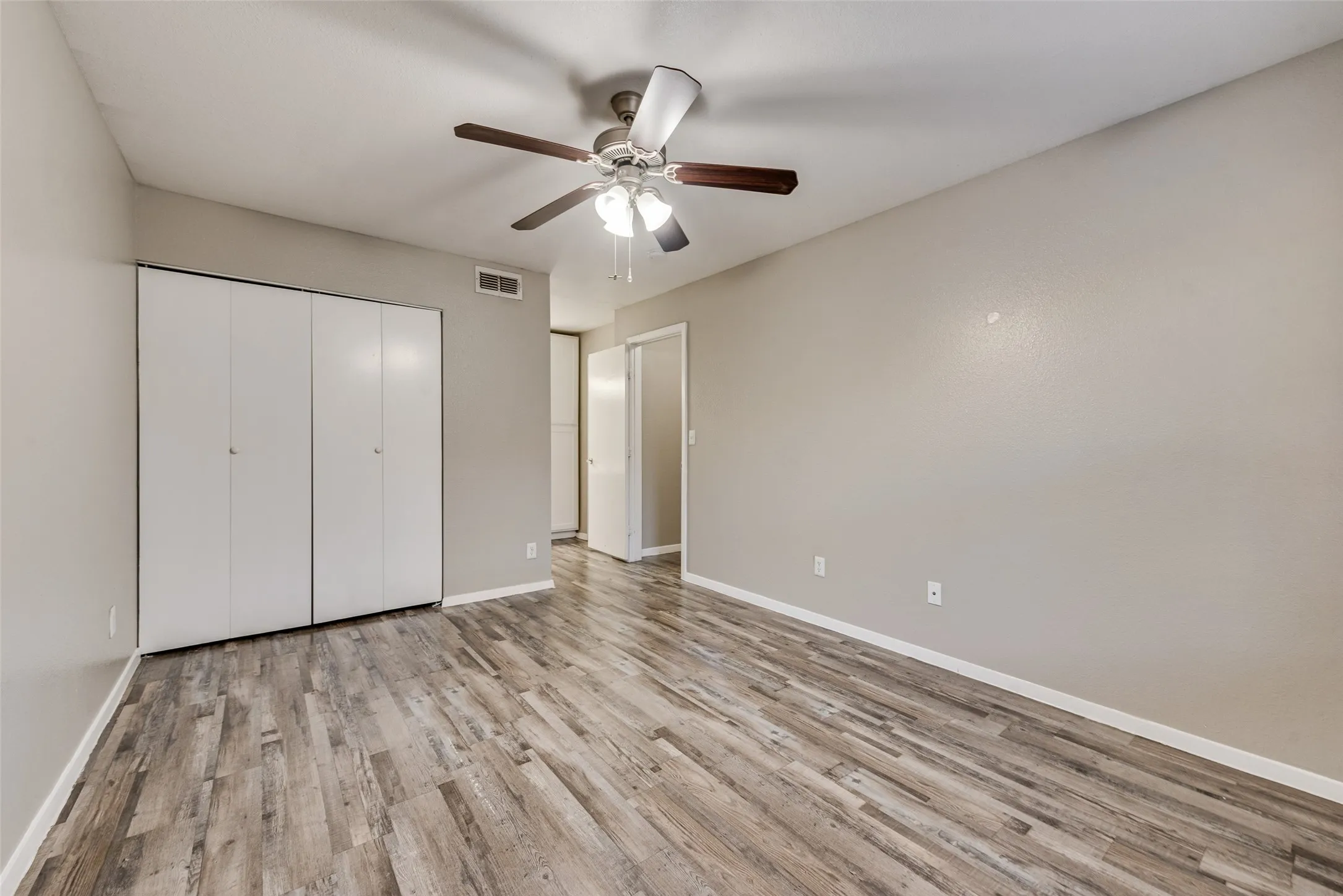 Spacious room with wood-finish flooring, light neutral wall paint, and a ceiling fan