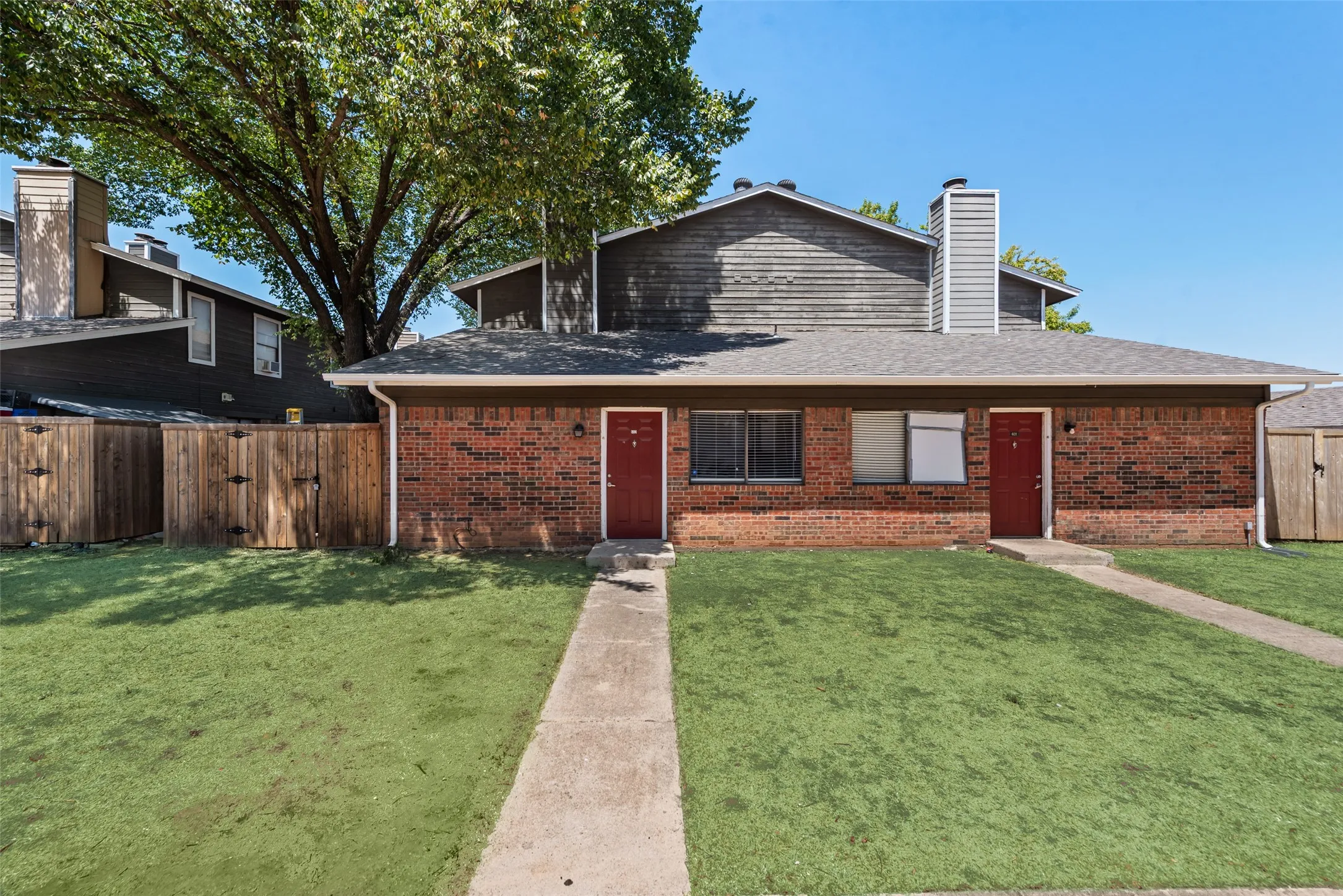 Brick exterior with a gray shingle roof, red entry doors, and a concrete walkway